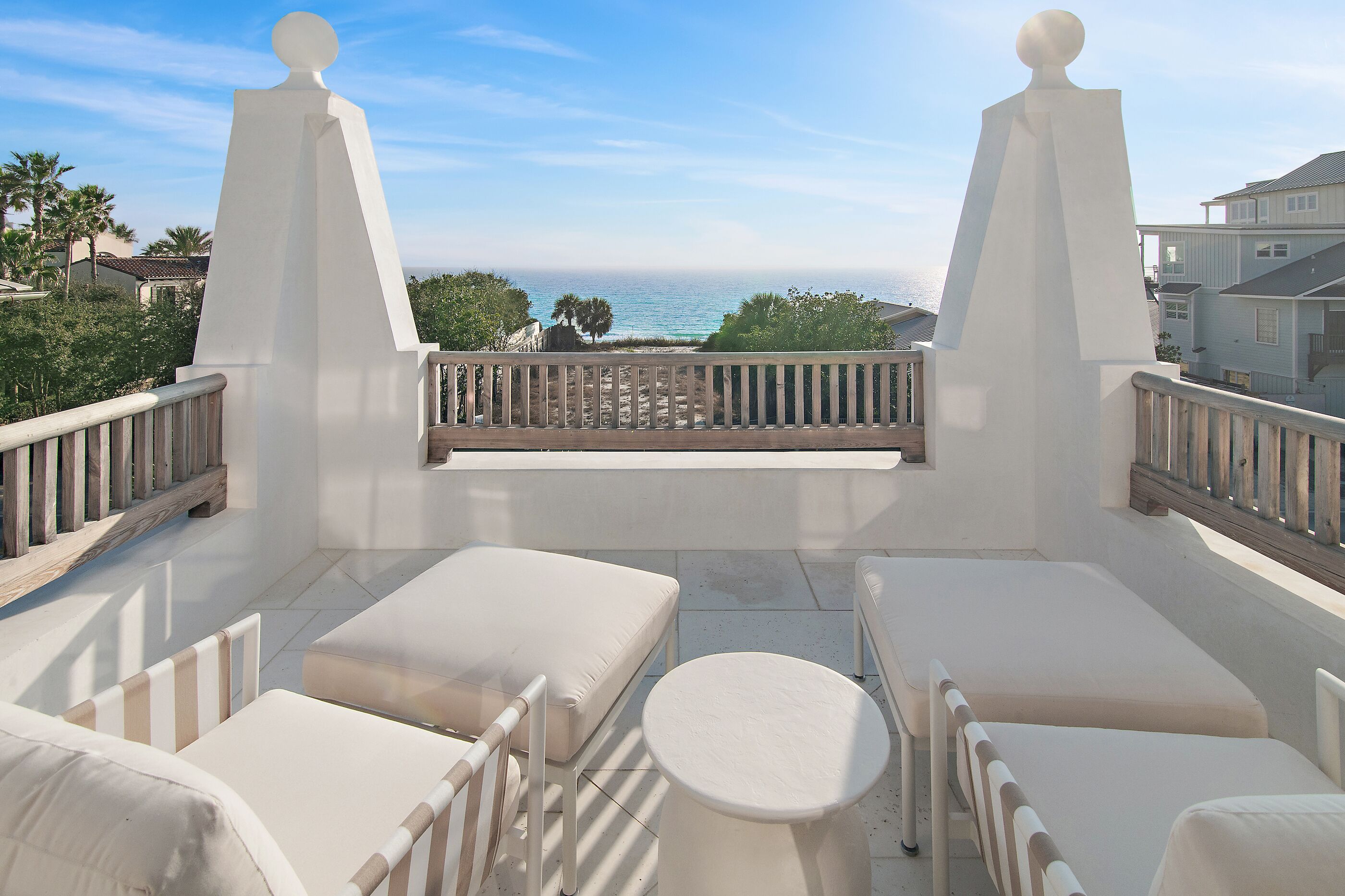 A balcony with white furniture, a view of the ocean, and a clear sky.