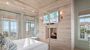 Une chambre dotée d’un grand lit, d’une cheminée, d’un téléviseur fixé au mur et offrant une vue sur la mer par les fenêtres.