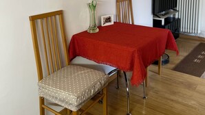 A dining area with a table covered in a red tablecloth, two wooden chairs with cushioned seats, a vase with flowers, and a framed picture on the wall. - MiniLevico (Levico Terme)