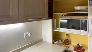 A kitchen with wooden cabinets, a microwave, a basket with jars, and a bottle of Amaretto. - MiniLevico (Levico Terme)