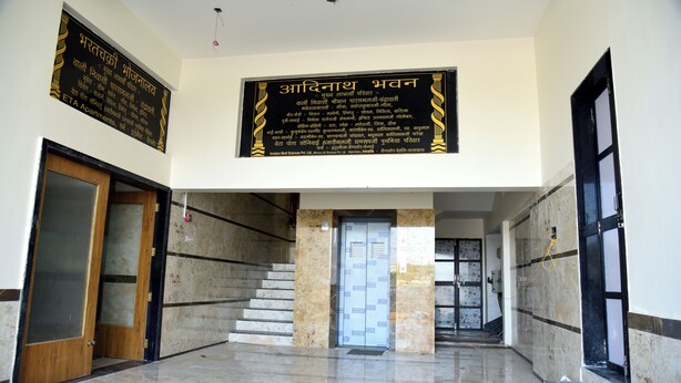A lobby with marble flooring, a staircase, and two signs in a foreign language. - Jainsite (Palitana)