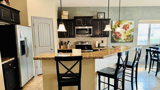 A modern kitchen with dark cabinets, a granite countertop, stainless steel appliances, and a central island with bar stools.