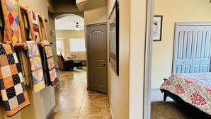 A hallway with a quilted wall hanging, a door, and a bed with a patterned bedspread.
