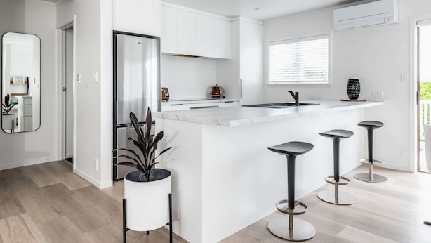 Een moderne keuken met witte kasten, een marmeren aanrechtblad en een centraal eiland met barkrukken.