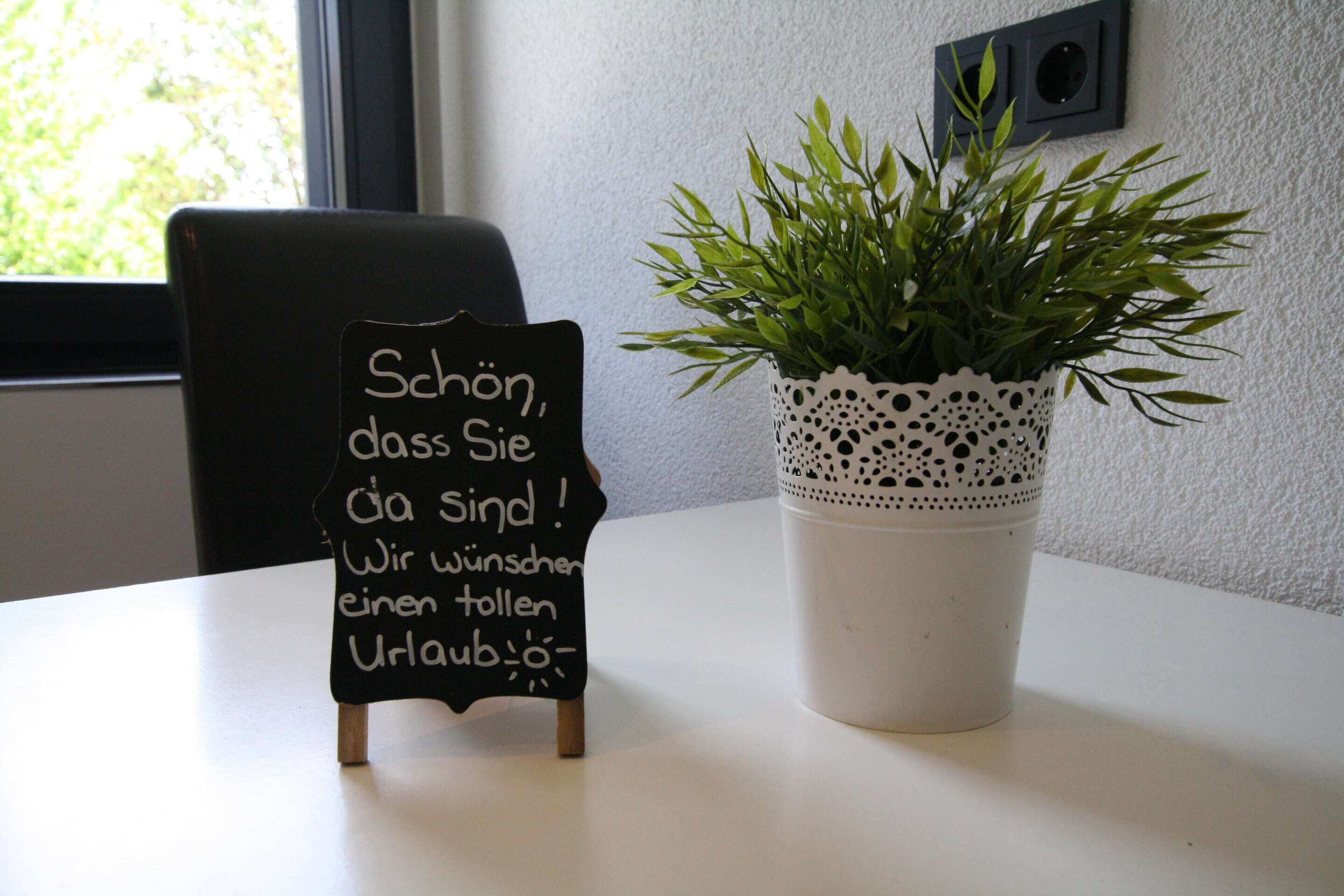 A small blackboard with handwritten text, a potted plant with a lace pot, and a chair.