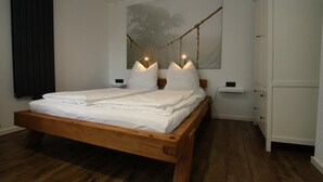 A neatly made wooden bed with white linens, a bedside table, a nightstand, and a wall-mounted lamp. - Ferienhaus Direkt an der Spree (Lübben (Spreewald))