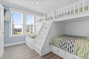 A bedroom with a bunk bed, a desk, and a window with blinds.