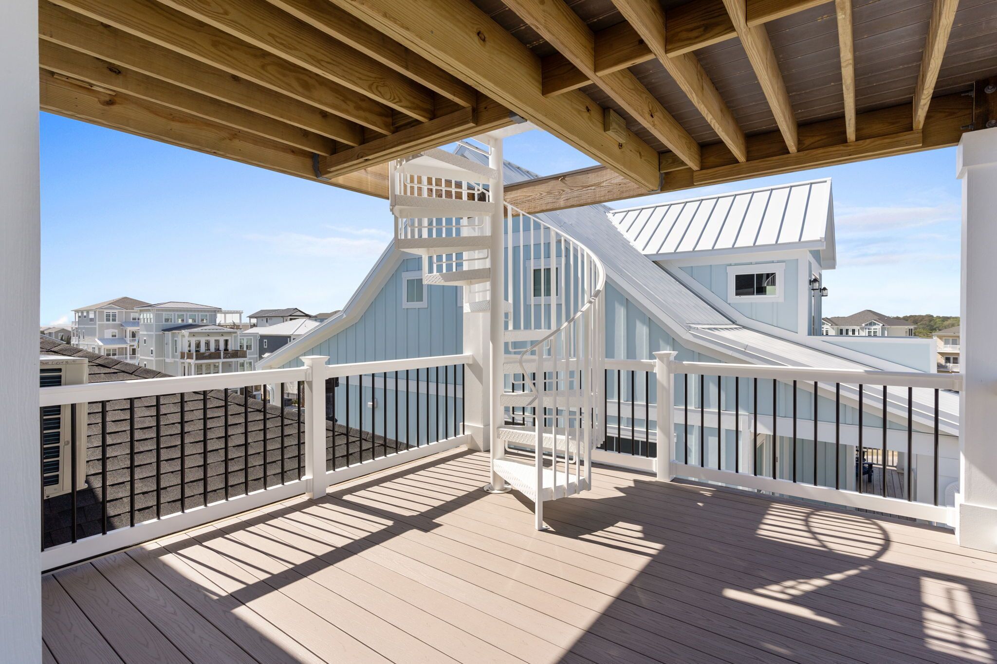 A wooden deck with a white railing, a spiral staircase, and a view of houses in the background.