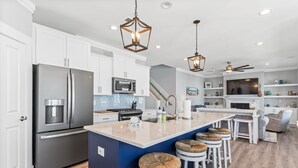 Una cocina moderna con armarios blancos, electrodomésticos de acero inoxidable, una isla grande con taburetes y luces colgantes.