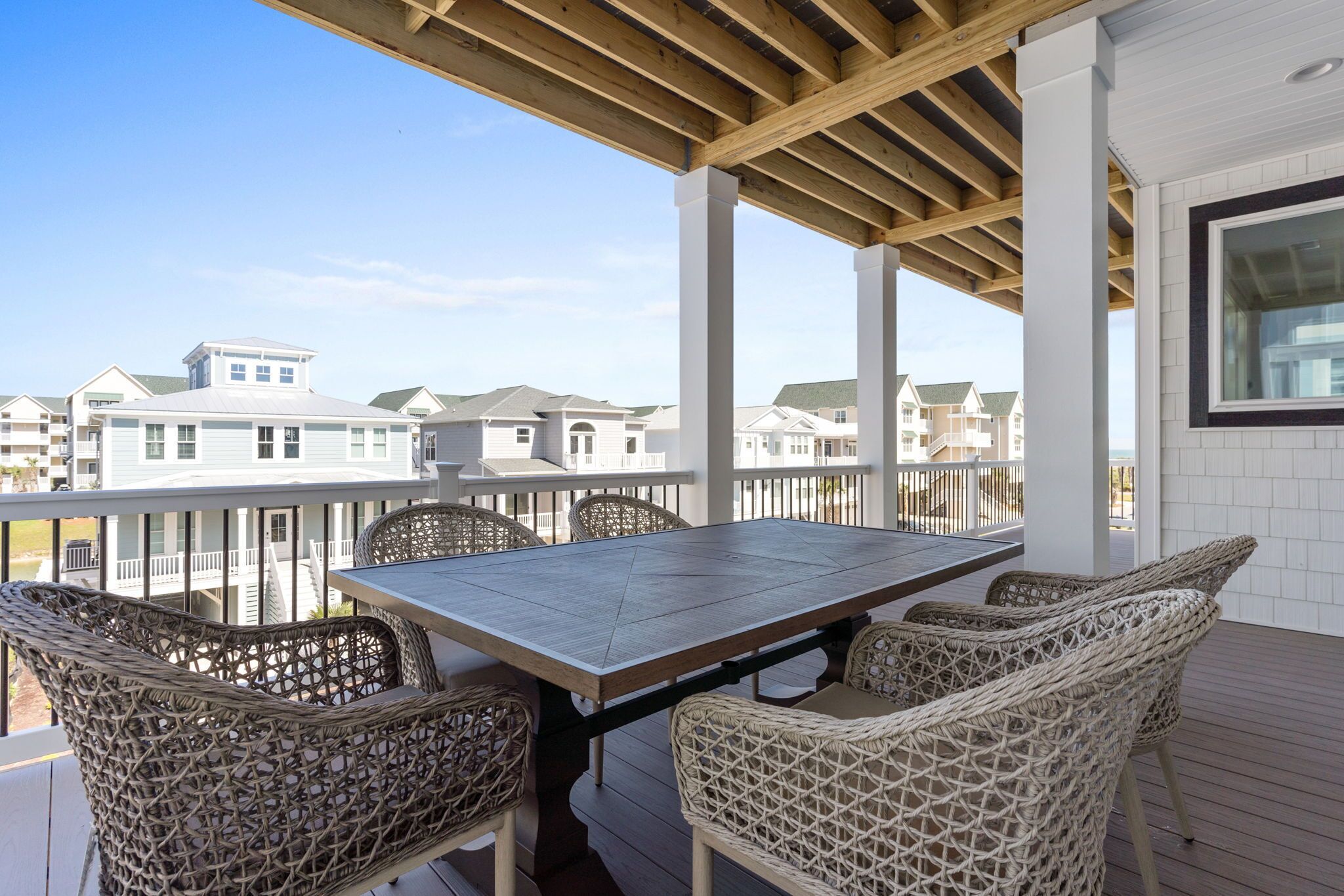 A covered outdoor patio with a table and wicker chairs, overlooking a residential area.