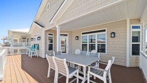A covered outdoor deck with a dining table and chairs, a white railing, and a view of the ocean. - Turtle by the Sea- 5 bedroom, 5+ bath, w/private pool & elevator, OIB resort. (Ocean Isle Beach)