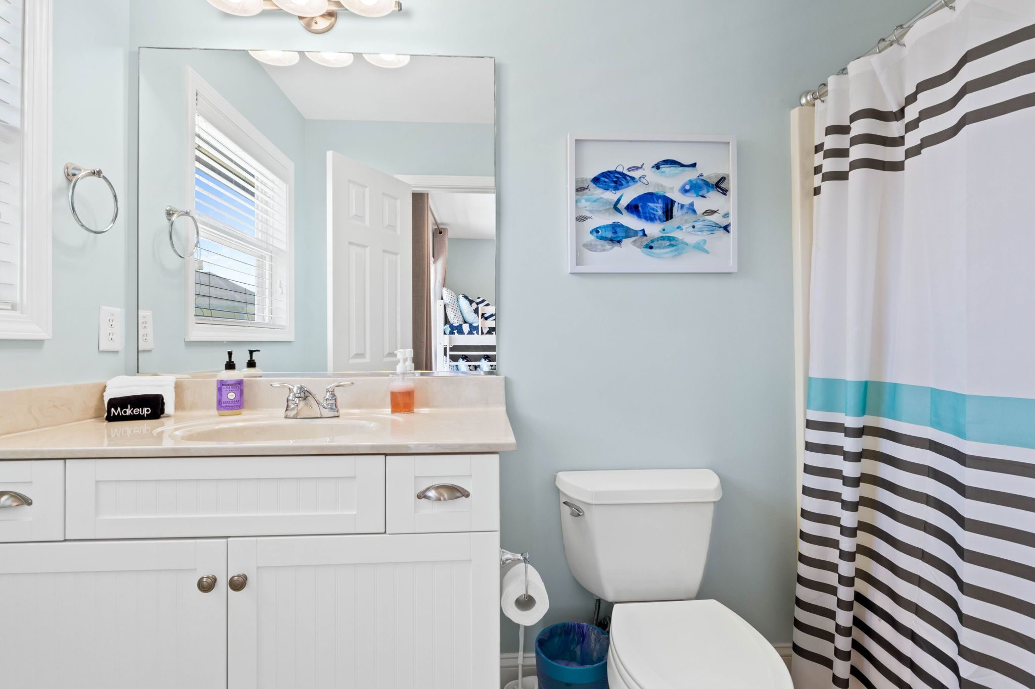 A bathroom with a white sink, a mirror, a toilet, and a striped shower curtain.