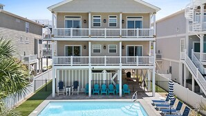 A multi-story hotel with a pool area, outdoor seating, and a staircase. - Turtle by the Sea- 5 bedroom, 5+ bath, w/private pool & elevator, OIB resort. (Ocean Isle Beach)