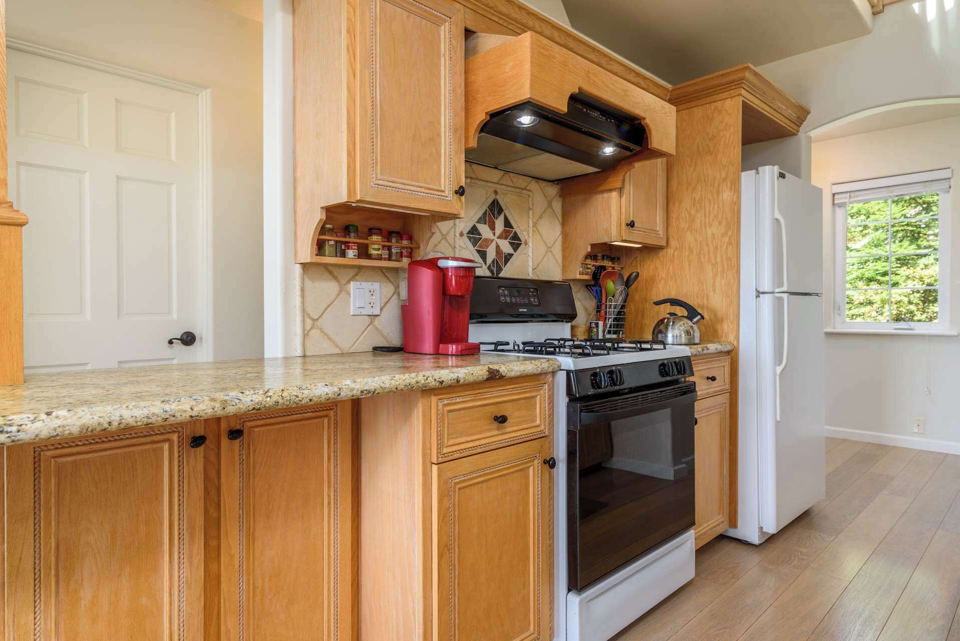 Una cocina con armarios de madera, encimera de granito, estufa a gas, horno y refrigerador.