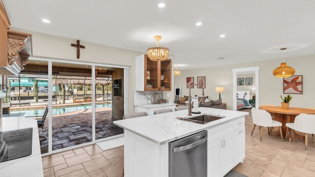A modern kitchen with a large island, a dining area with a wooden table, and a view of a swimming pool. - Dreamers Hideaway I Waterfront I Direct Access (Naples)