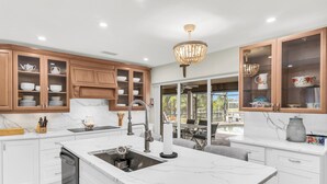 A modern kitchen with white marble countertops, wooden cabinets, and a central island. - Dreamers Hideaway I Waterfront I Direct Access (Naples)