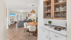 A modern kitchen with white cabinetry, a wooden dining table, and a built-in glass cabinet with decorative items. - Dreamers Hideaway I Waterfront I Direct Access (Naples)