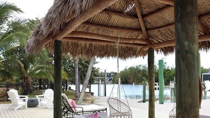 A wooden deck with a thatched roof, white lounge chairs, and a hanging chair. - Dreamers Hideaway I Waterfront I Direct Access (Naples)