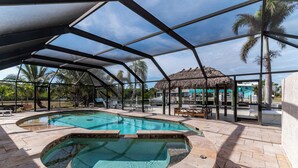 A covered swimming pool with a hot tub, lounge chairs, and a thatched-roof structure. - Dreamers Hideaway I Waterfront I Direct Access (Naples)