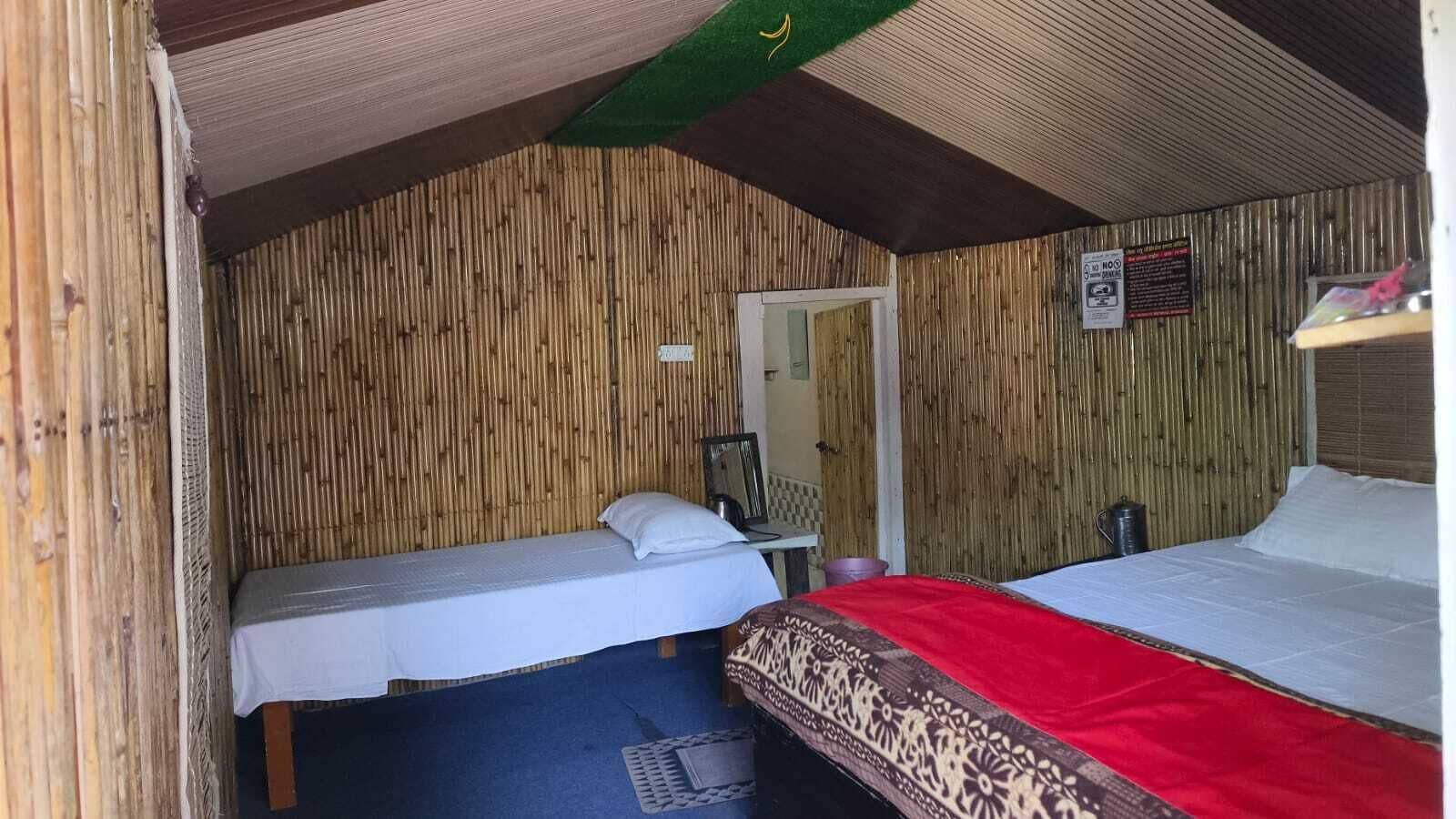 Ein Zimmer mit zwei Betten, eines mit roter Bettdecke und das andere mit weißer Bettdecke. Eine Holzwand und ein kleiner Tisch mit einem Stuhl sind ebenfalls vorhanden.