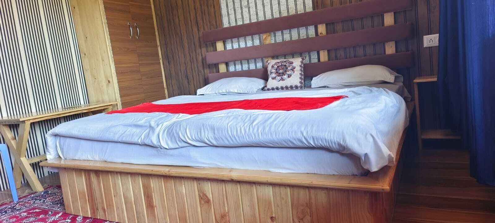Una cama de madera con una colcha roja, almohadas blancas y un cojín decorativo.