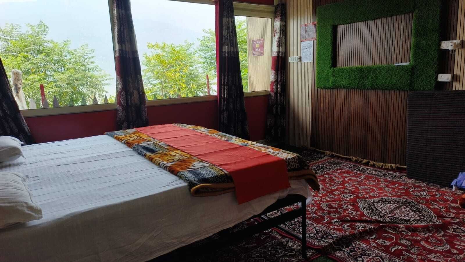 A room with a bed, a window with curtains, a green wall, and a patterned rug.