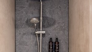 Ein modernes Duschsystem mit Regendusche, Handbrause und verschiedenen Duschzubehörteilen, ergänzt durch zwei Flaschen Wellnessprodukte.