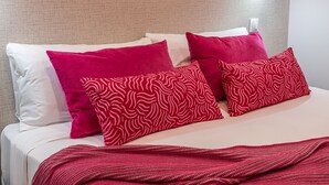 Ein Bett mit weißen und roten Kissen, einer roten Decke und einer strukturierten Wand im Hintergrund.