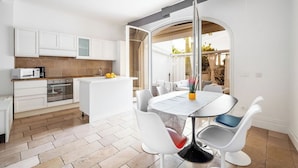 A modern kitchen with white cabinetry, a central island, and a dining area with a round table and white chairs. - Casa Malu (Positano)