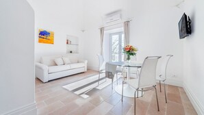 A modern living room with a white sofa, a glass dining table, and a TV mounted on the wall. - Casa Malu (Positano)