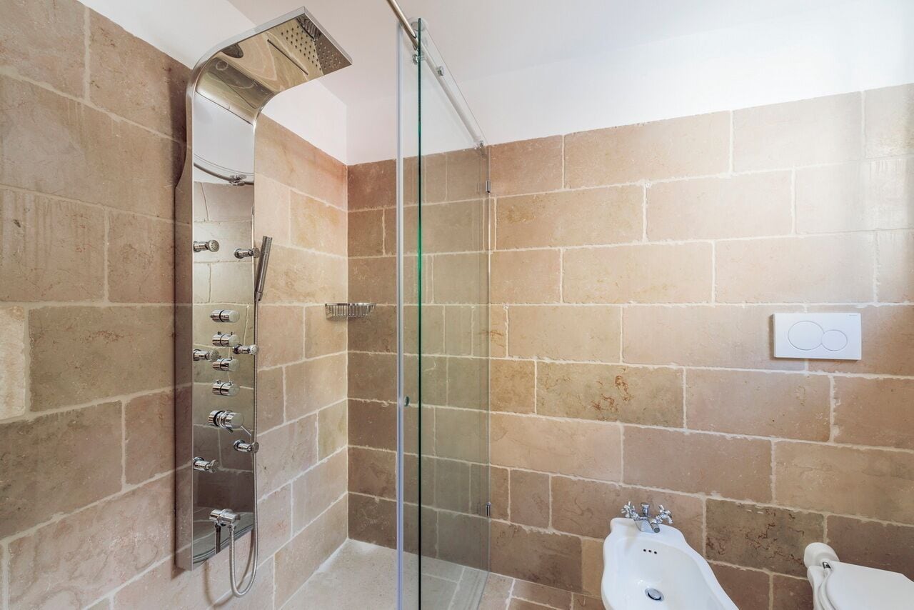 A modern bathroom with a glass-enclosed shower, a wall-mounted sink, and beige tiled walls.