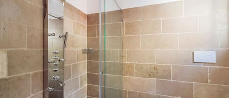 A modern bathroom with a glass-enclosed shower, a wall-mounted sink, and beige tiled walls.
