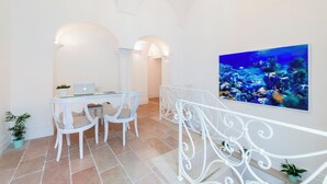 A dining area with a white table and chairs, a laptop, and a large painting of an underwater scene. - Casa Malu (Positano)
