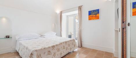 A bedroom with a bed, a glass shelf, a door, and a painting on the wall.
