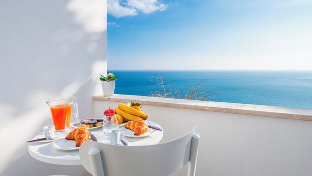 A breakfast setup with croissants, bananas, and juice on a balcony overlooking the sea. - Casa Malu (Positano)