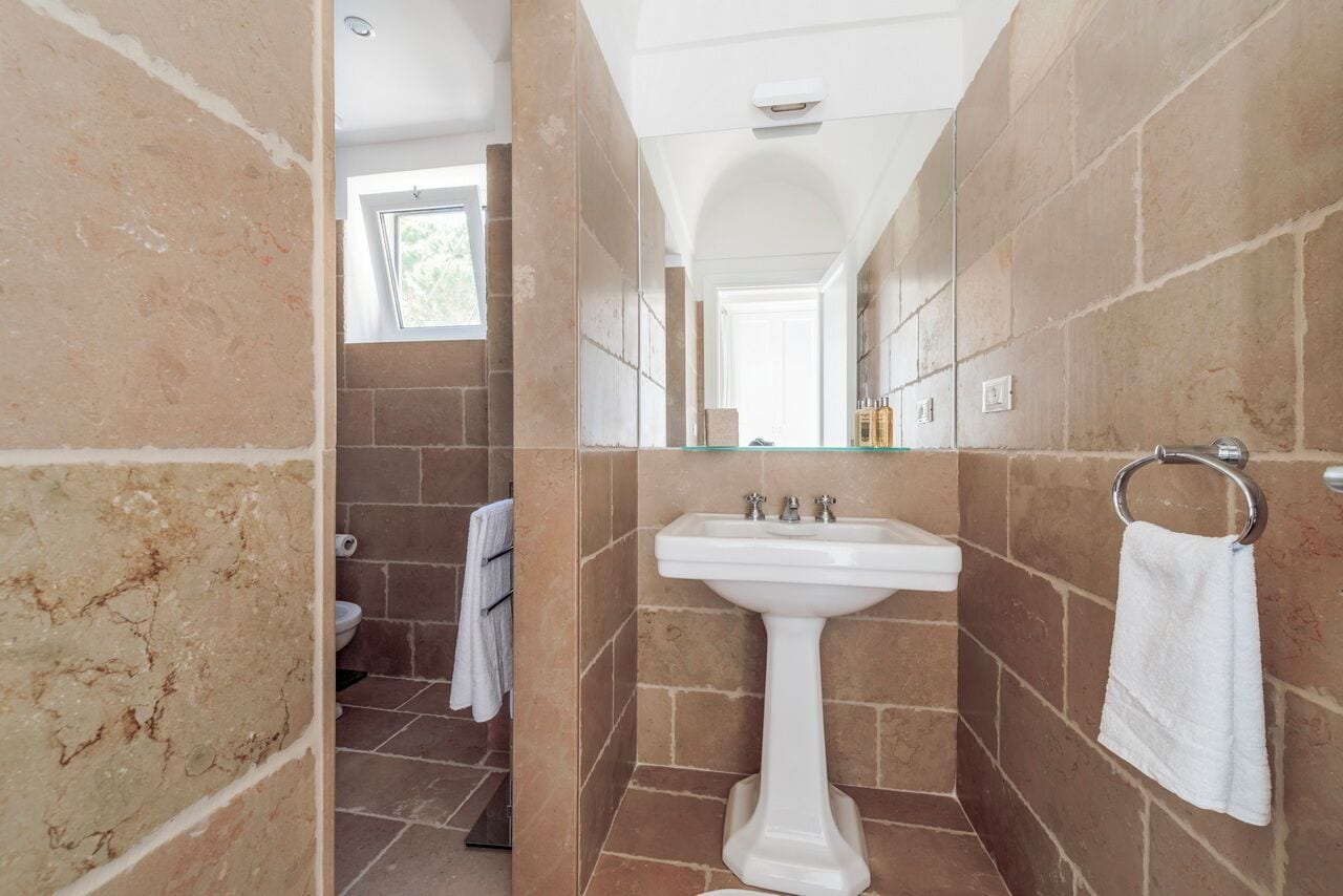 A bathroom with a pedestal sink, tiled walls, a window, and a towel rack.