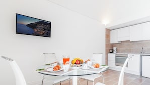 A modern kitchen with white cabinets, a dining area with a glass table, and a scenic view of a coastal town at dusk. - Casa Malu (Positano)