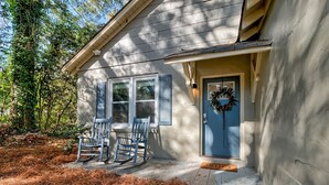 Une maison avec une porte bleue, deux fauteuils à bascule et un porche recouvert de feuilles de pin.