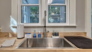 Une cuisine avec un évier en acier inoxydable, une fenêtre au-dessus et un tapis noir sur le plan de travail.