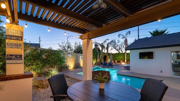 An outdoor patio with a pool, wicker chairs, and a table with a vase. - Mirage Oasis: Pool & Hot Tub [Free Spa Heating + Early Check-In] (Indio)