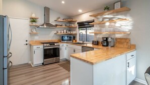 A modern kitchen with white cabinets, stainless steel appliances, wooden countertops, and built-in shelves. - Mirage Oasis: Pool & Hot Tub [Free Spa Heating + Early Check-In] (Indio)