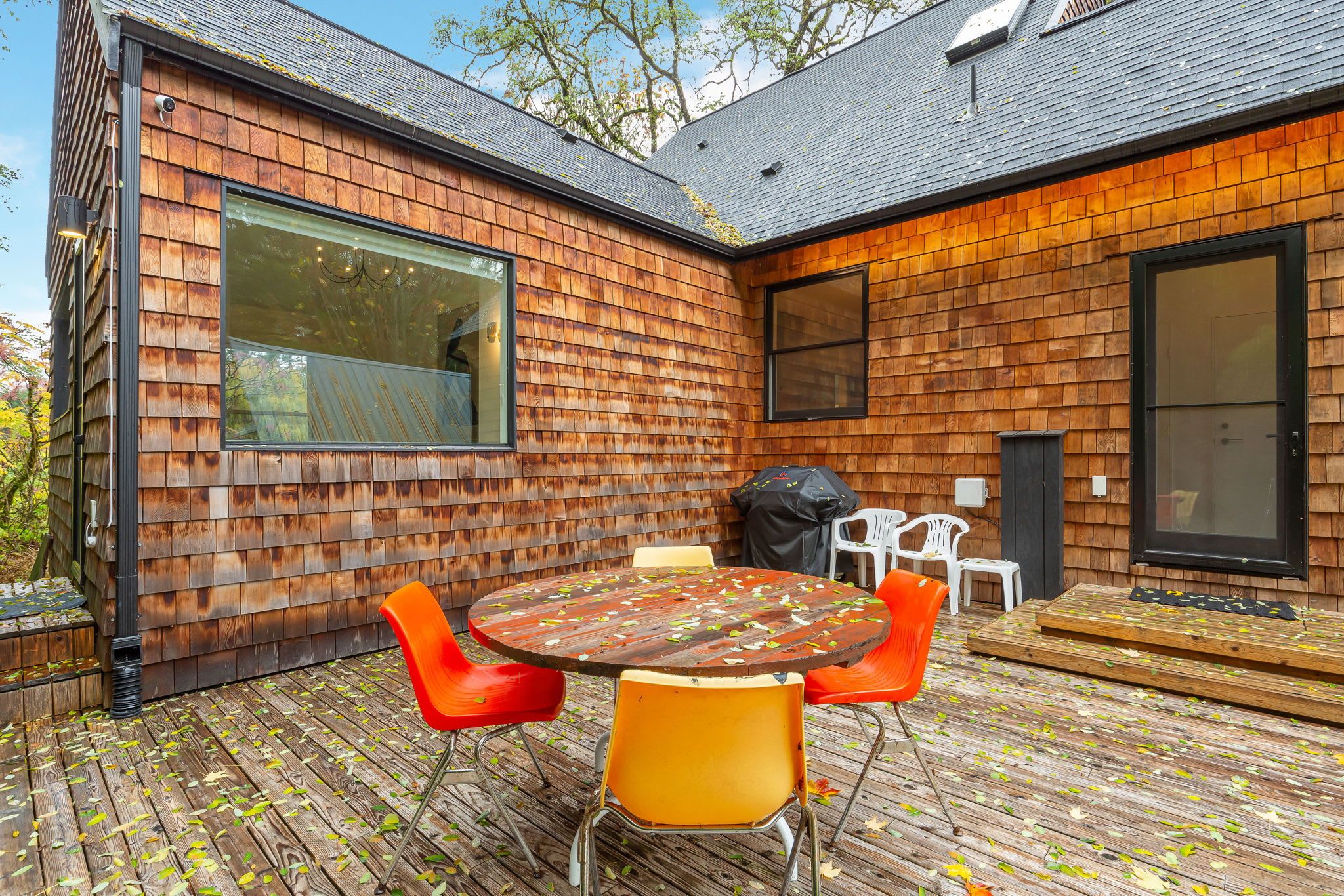 A modern house with a wooden exterior, a large window, and a deck with outdoor furniture.