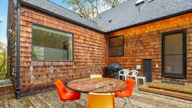Una casa moderna con fachada de madera, un ventanal grande y una terraza con mobiliario exterior.