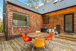 Een modern huis met een houten gevel, een groot raam en een terras met tuinmeubilair.