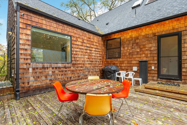 Una casa moderna con fachada de madera, un ventanal grande y una terraza con mobiliario exterior.