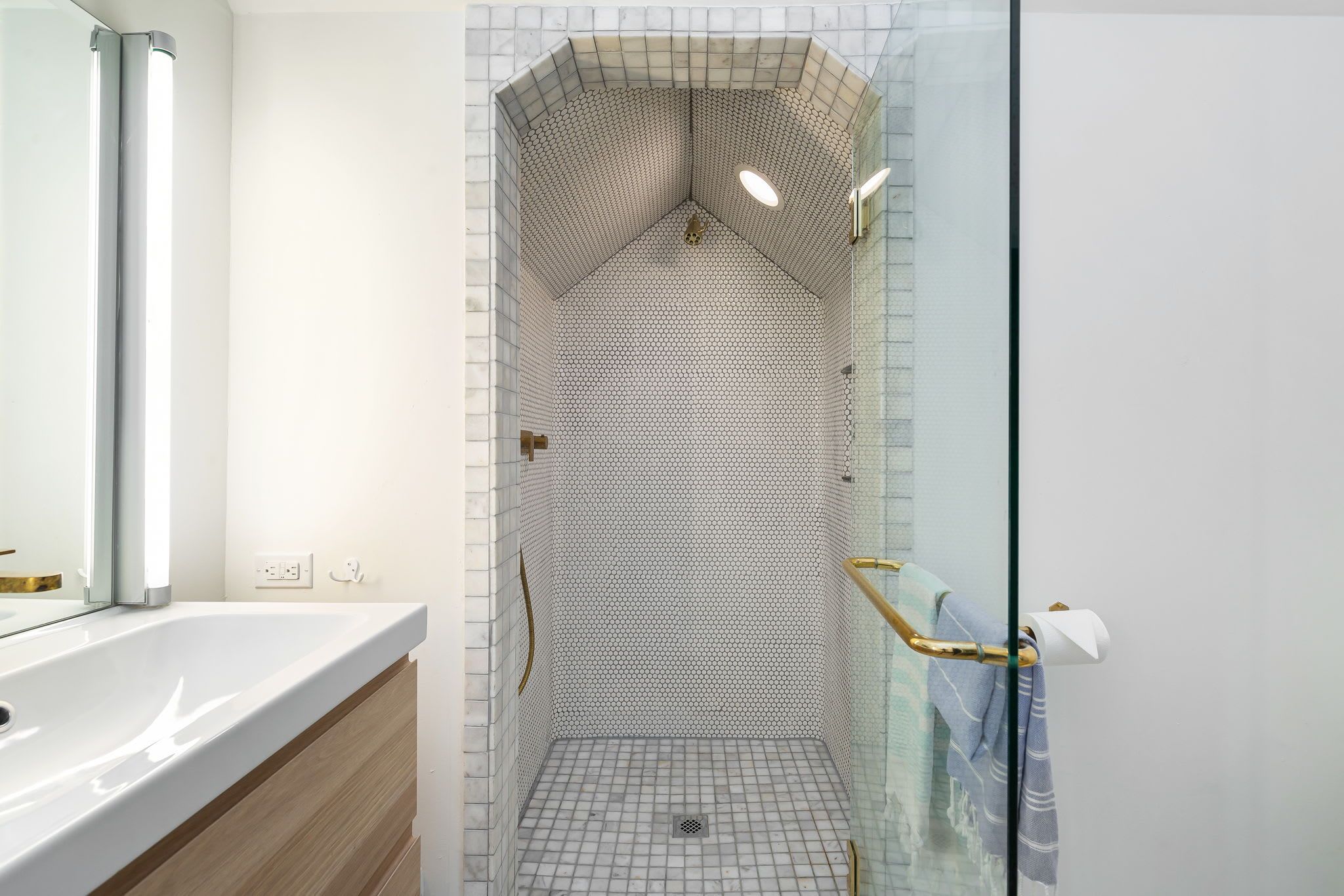A modern bathroom with a glass shower enclosure, a white sink, and a wooden vanity.