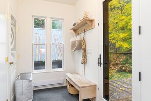 Ein helles, modernes Badezimmer mit einer Sitzbank, einem Holzregal mit Haken und Blick auf einen Garten durch ein Fenster.