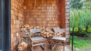 A wooden deck with two chairs and a stack of firewood. - Sleeps 6 · 3BR Craftsman · Mountain Views · Near Skagit River (Concrete)