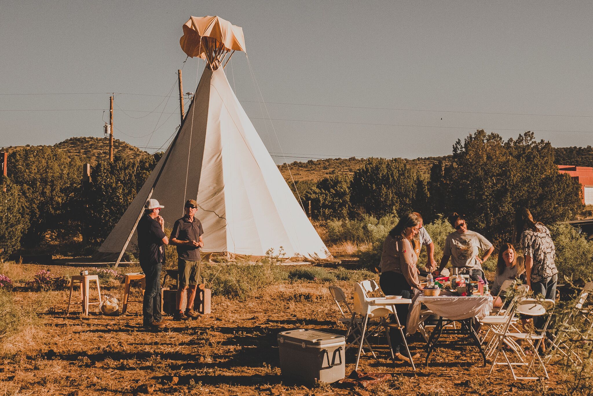 A group of people gathered around a table with a tent in the background.