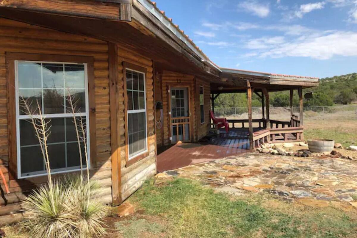 Une cabane en rondins avec un patio en pierre et une véranda couverte.